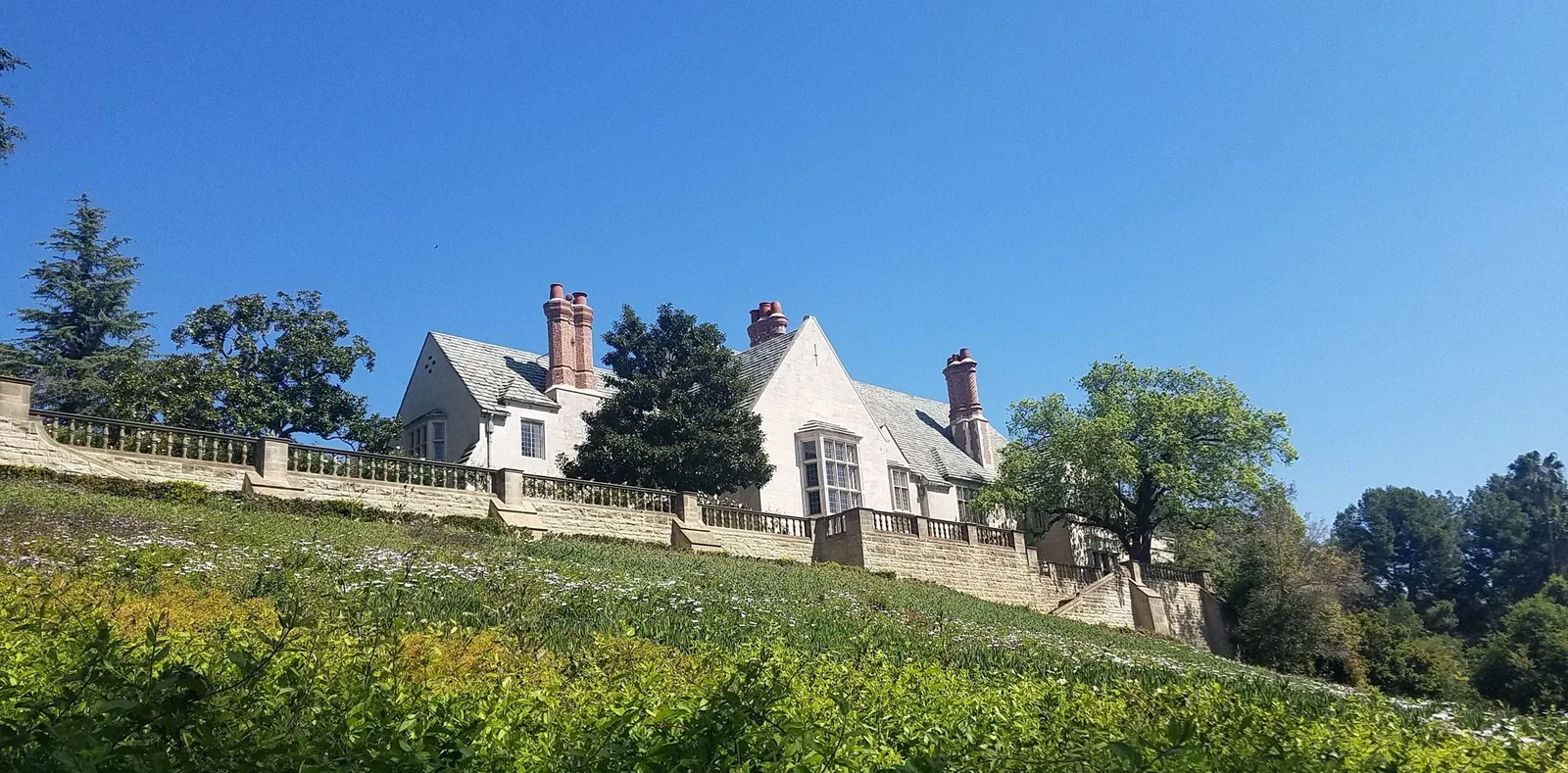 Tudor style stone mansion behind a lawn and balustrade