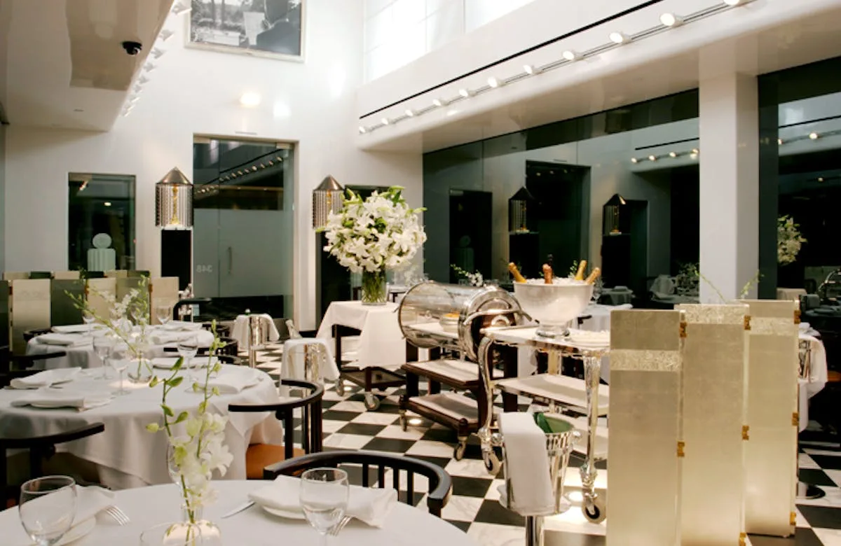 White-clothed dining room with a checkerboard floor and floral arrangements