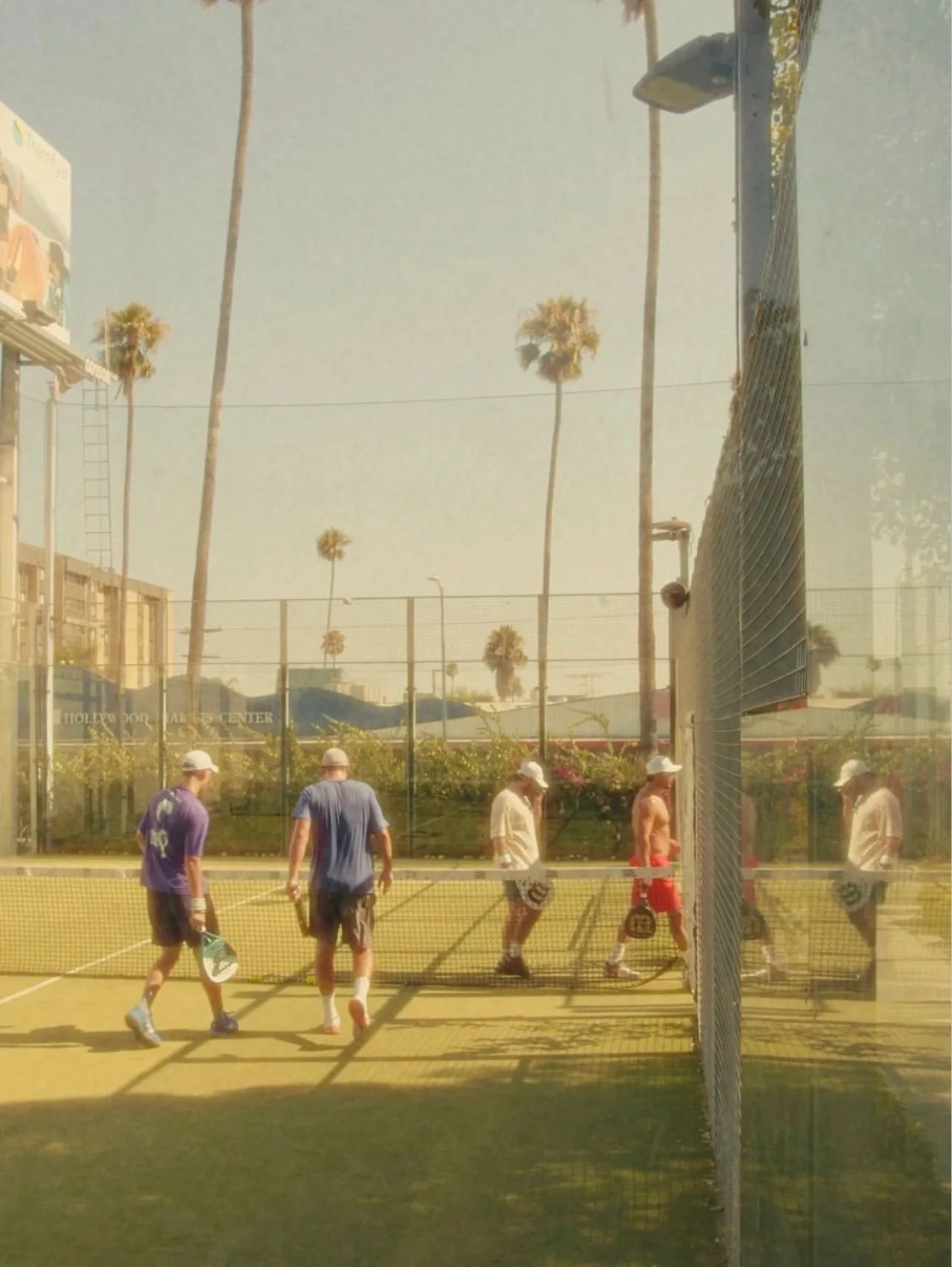 Players on an enclosed padel court under palm trees