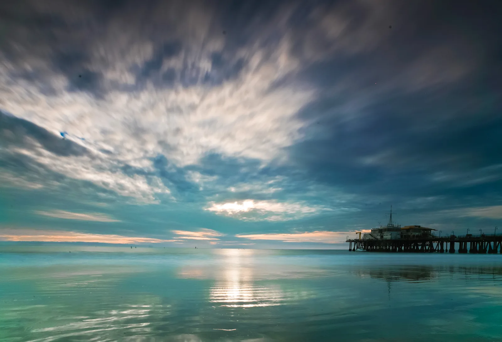 Wide dusk sky over calm water with a distant pier silhouette