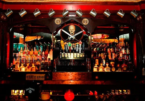 Nautical themed bar under red light with a skull banner above bottles