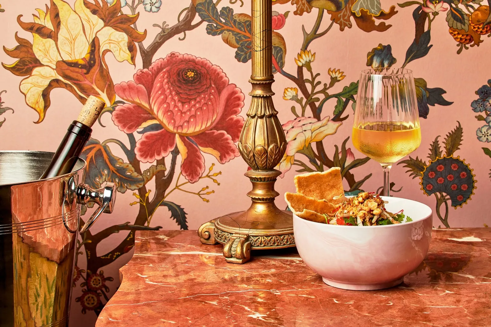 Noodle bowl and a beer on a table against floral wallpaper