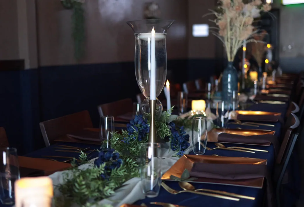 Candlelit long table set with glassware and dark napkins