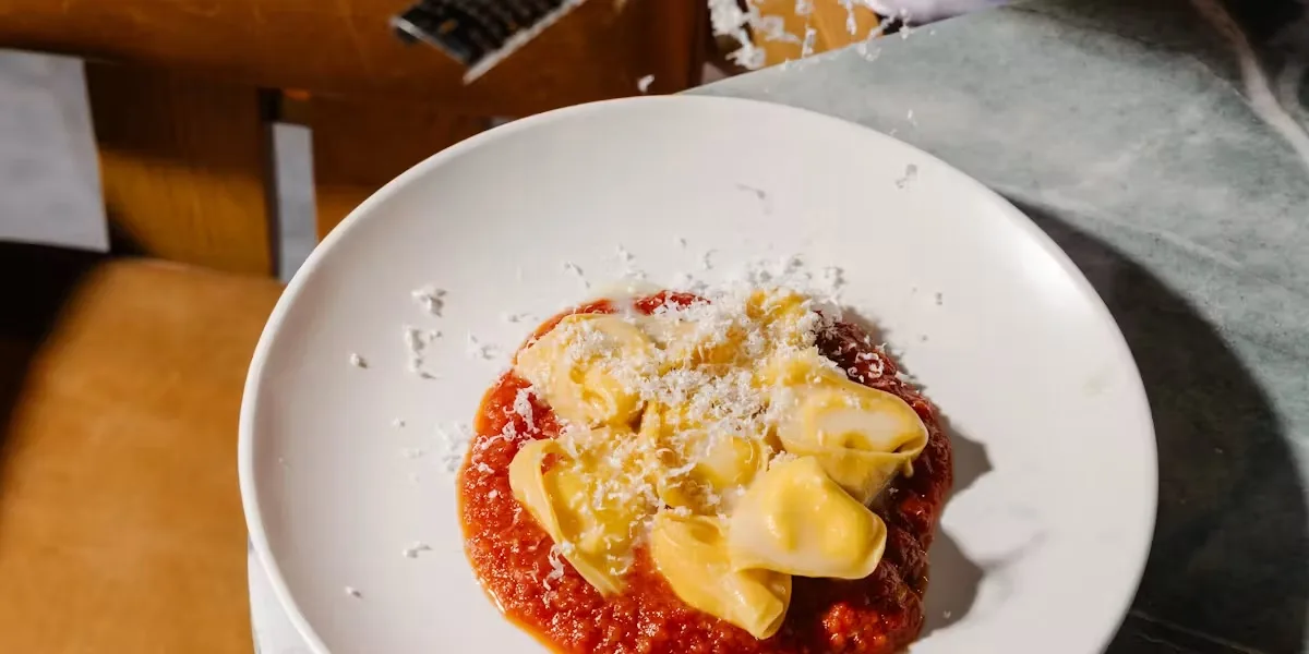 Pasta shells in tomato sauce with shaved cheese on a white plate