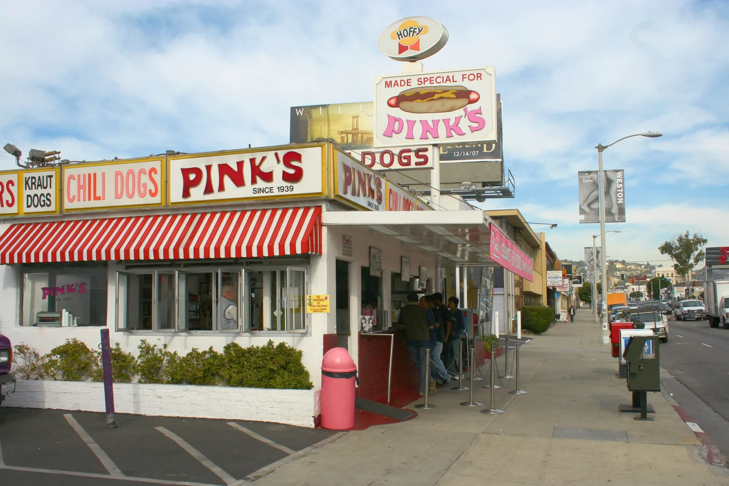 Corner hot dog stand with striped awning and roadside signs