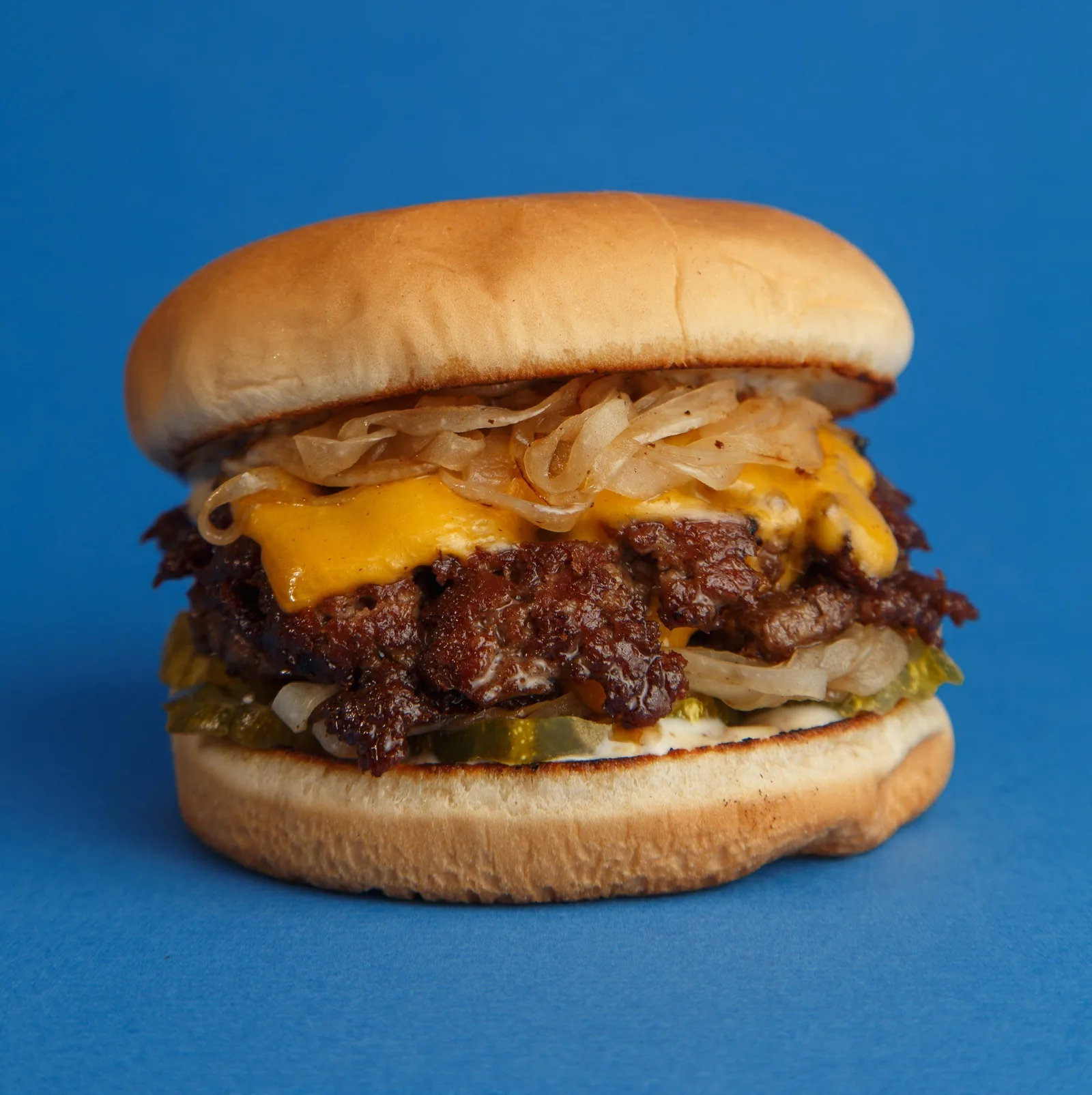 Double cheeseburger with grilled onions shot against a bright blue backdrop