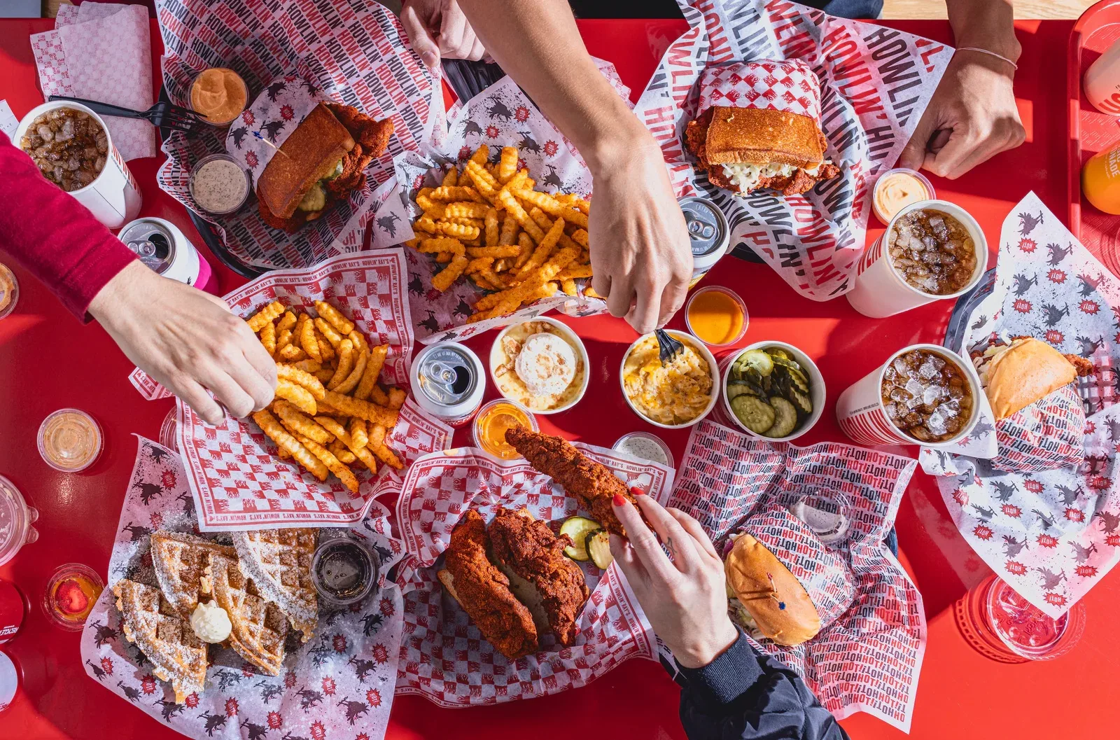 Overhead view of hands reaching over fried chicken and fries