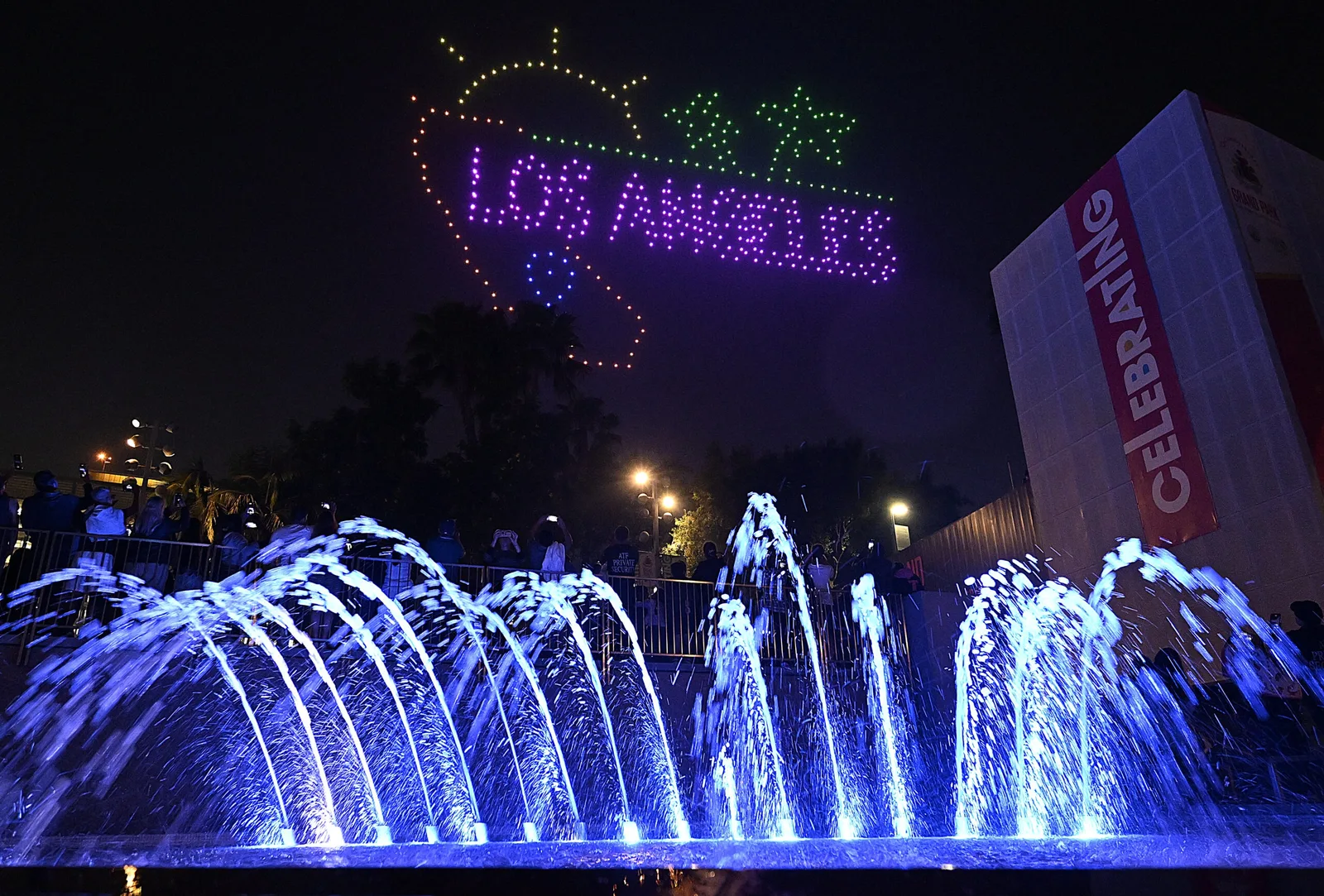 Illuminated fountain jets at night below a lit Los Angeles sign