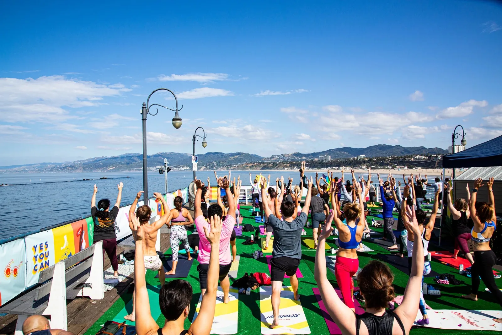 Outdoor yoga class raising arms on green mats beside the ocean