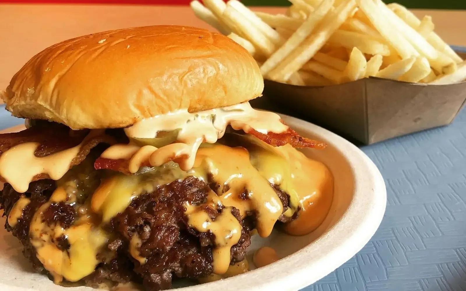 Saucy smashburger on a plate beside a paper boat of fries