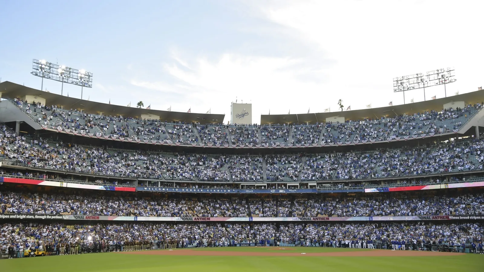 Packed stadium tiers under bright sky, outfield grass visible at bottom