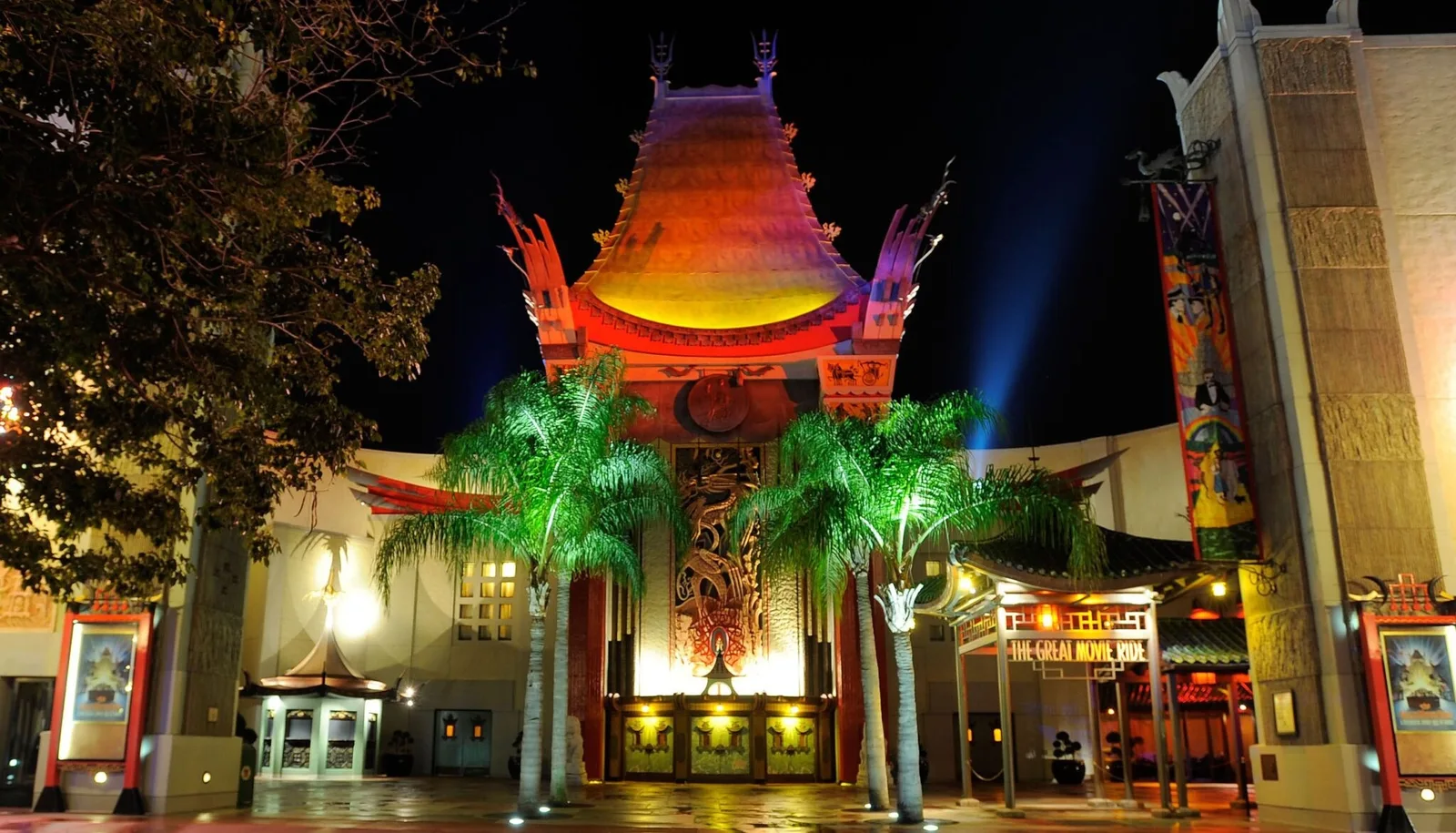 Pagoda style theatre facade lit at night with palms and a marquee