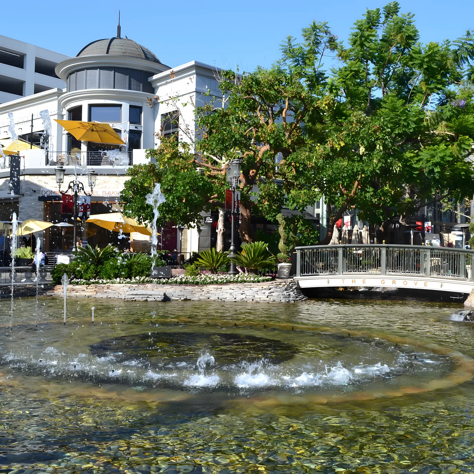 Fountain jetting in front of shopfronts with awnings and trees