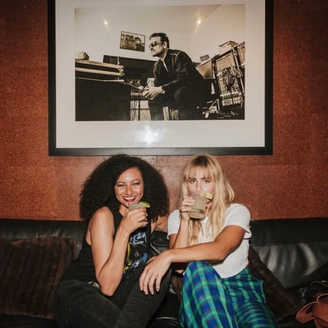 Two women laughing with drinks in a booth beneath framed artwork