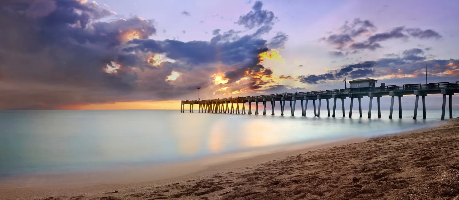 The pier stretching into calm water under a pink sunset