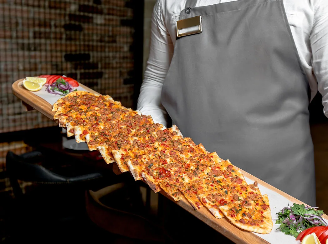 Server in an apron holding a long flatbread topped with minced meat