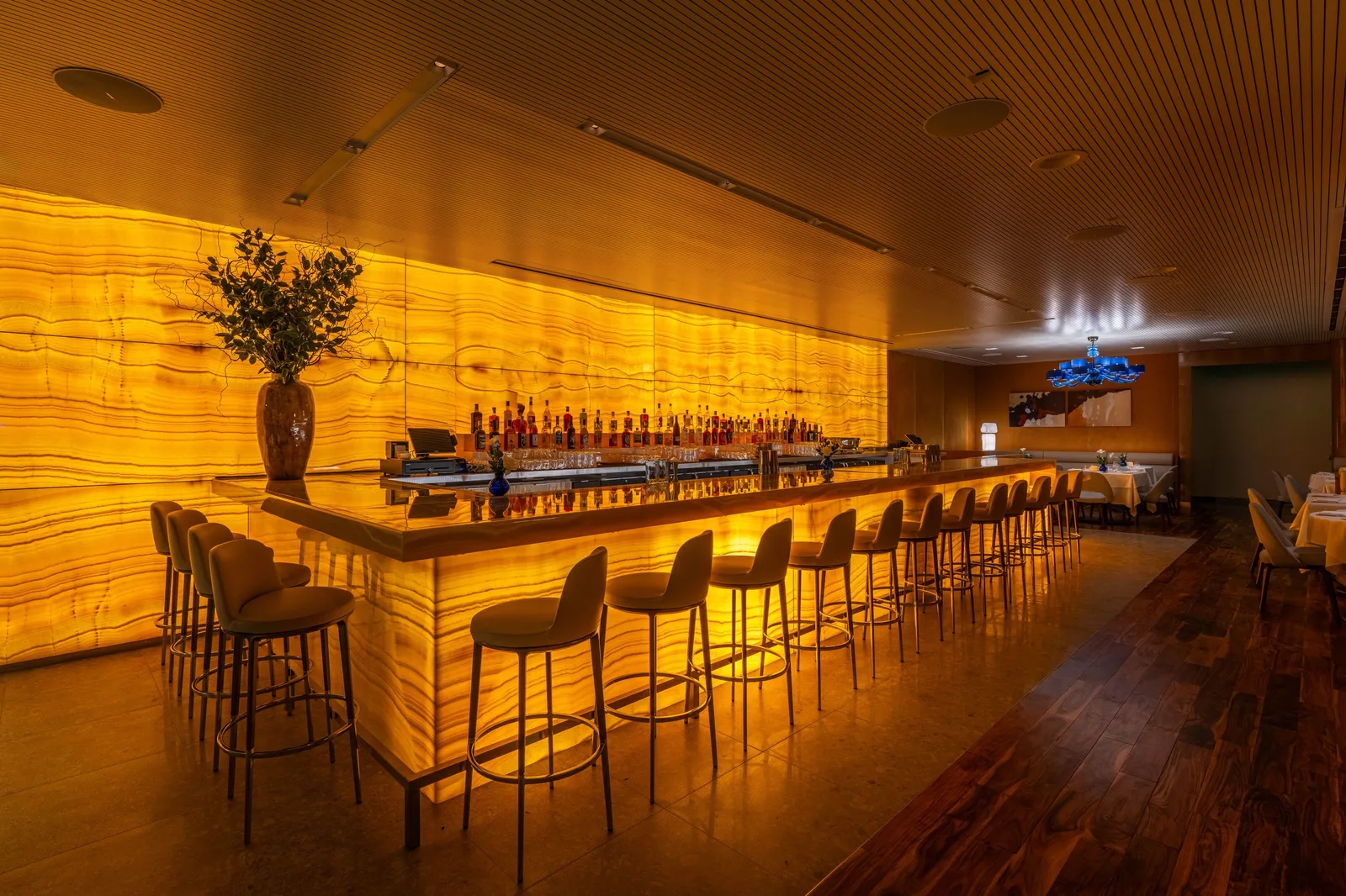 Warmly lit bar with a backlit counter and a row of stools