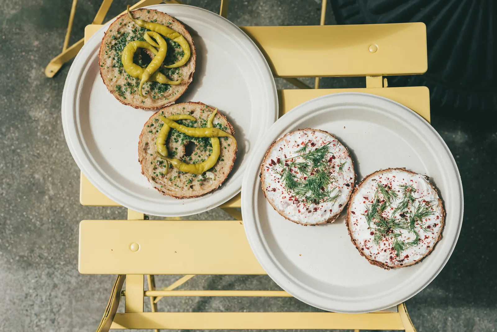 Two plates of topped bagel halves on a yellow metal chair