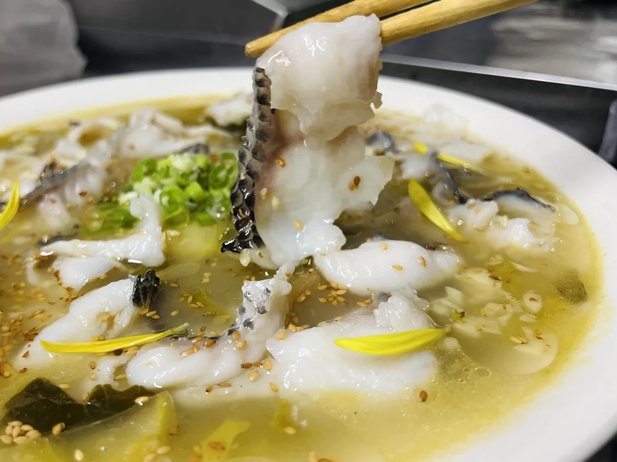 Chopsticks lifting poached fish from a bowl of pale green broth