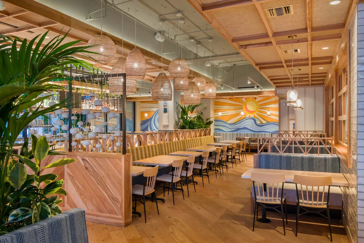 Airy restaurant interior with wood floors, plants and a wave mural