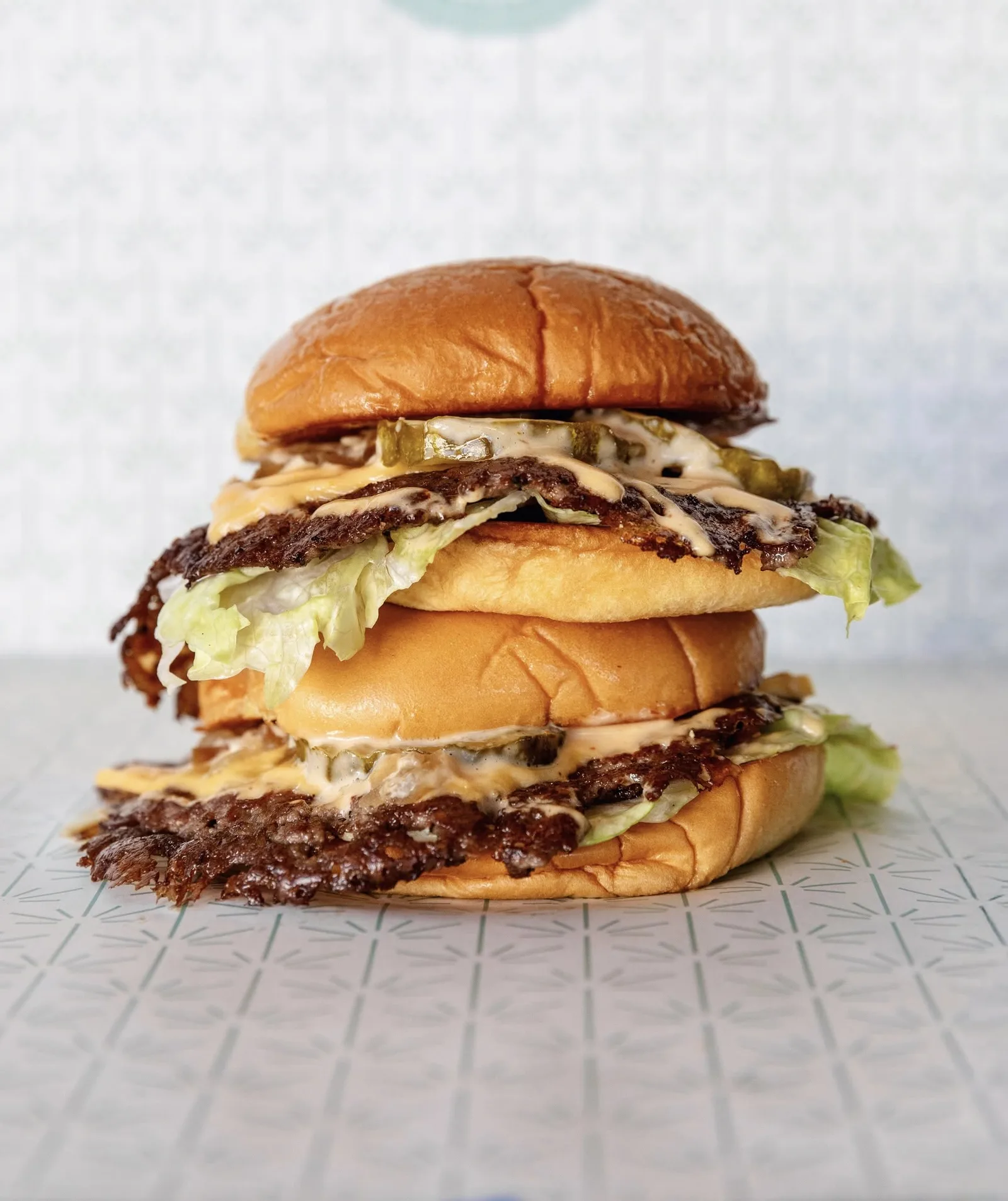 Tall double cheeseburger with lettuce on a sesame seed bun