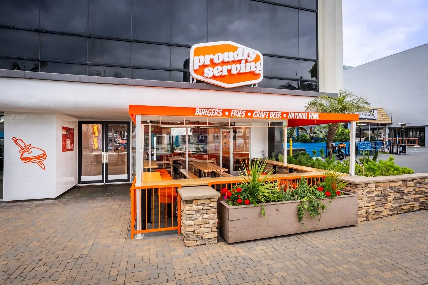 Burger restaurant exterior with lit signage and planters out front