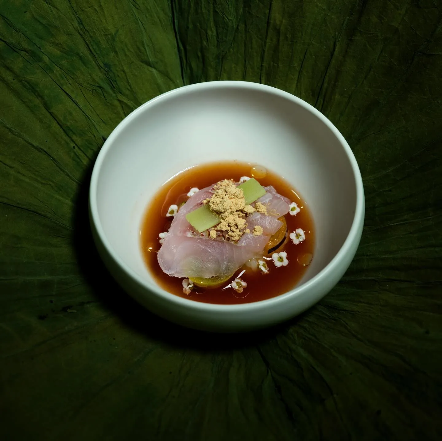 Sliced raw fish in broth topped with a grated garnish