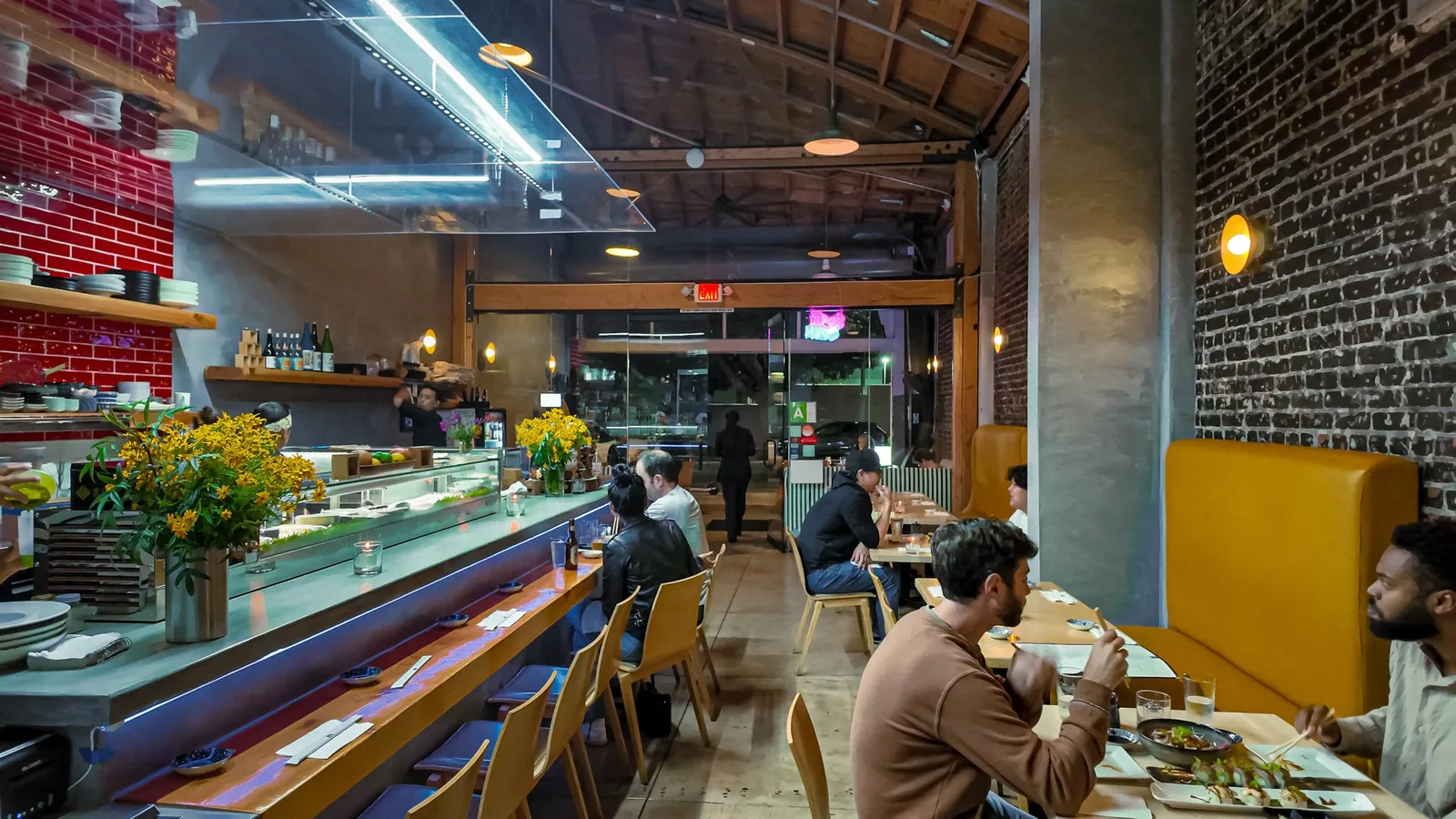 Diners eating at a sushi counter beside a chilled display case