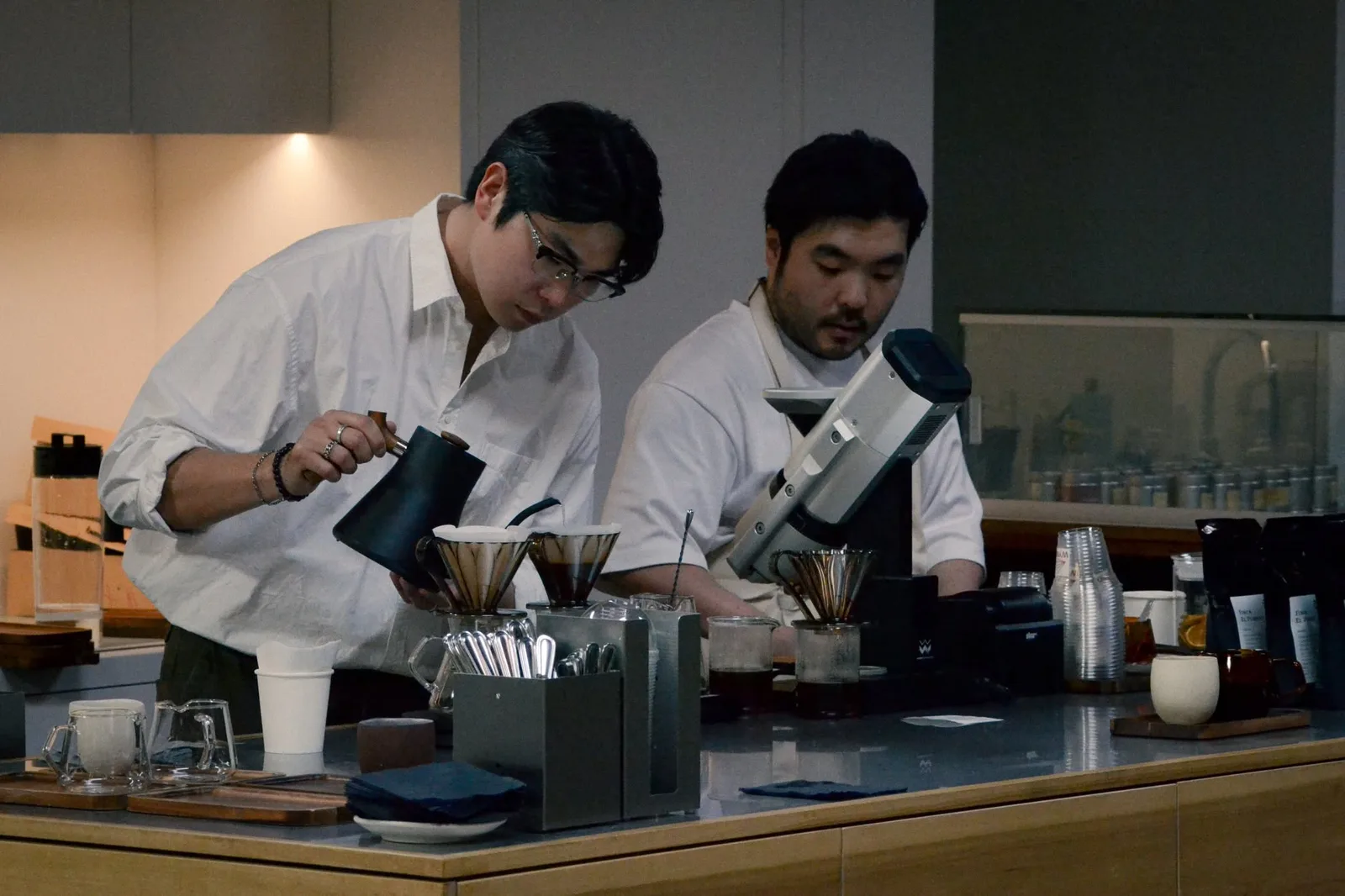Two baristas pouring filter coffee behind a cafe counter