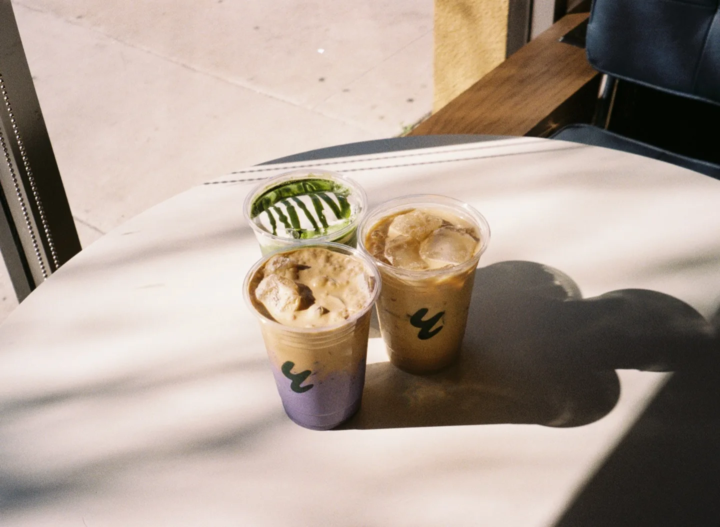 Two iced drinks in plastic cups on a sunlit table