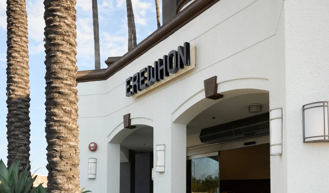 White stucco storefront with lettered signage and a palm tree