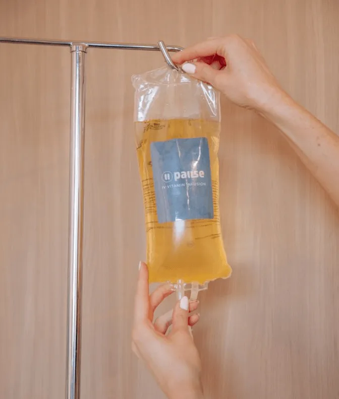 Hand holding an IV drip bag filled with pale yellow fluid