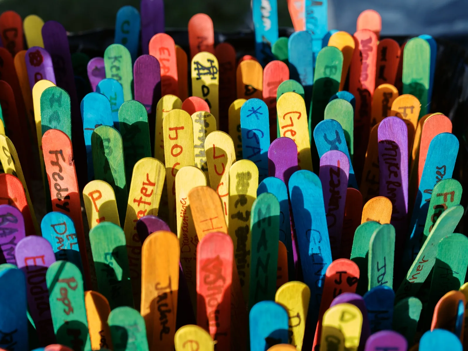 Dense rows of brightly painted wooden markers with handwriting