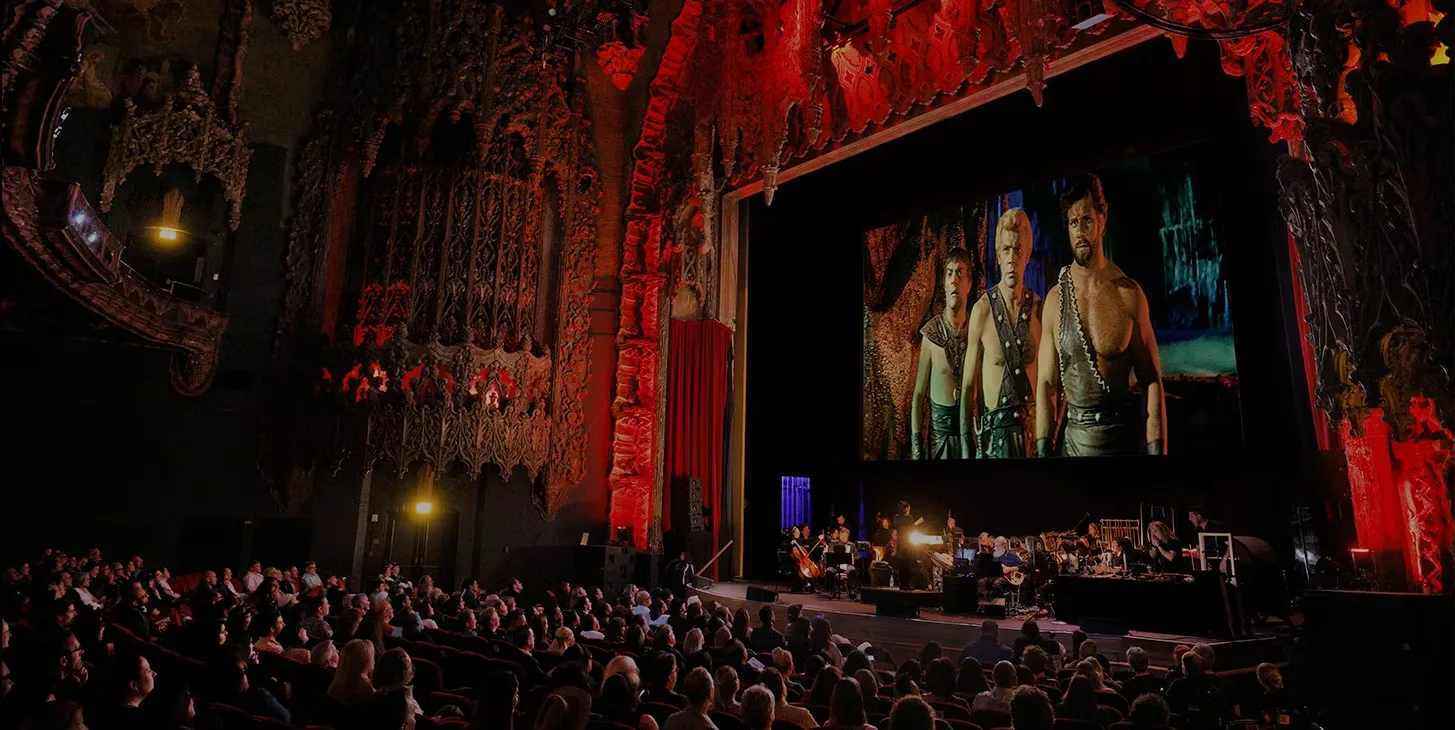 Audience in an ornate theatre watching a film with live orchestra