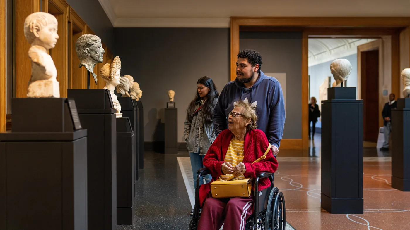 Visitors moving through a gallery of classical busts at a Los Angeles museum