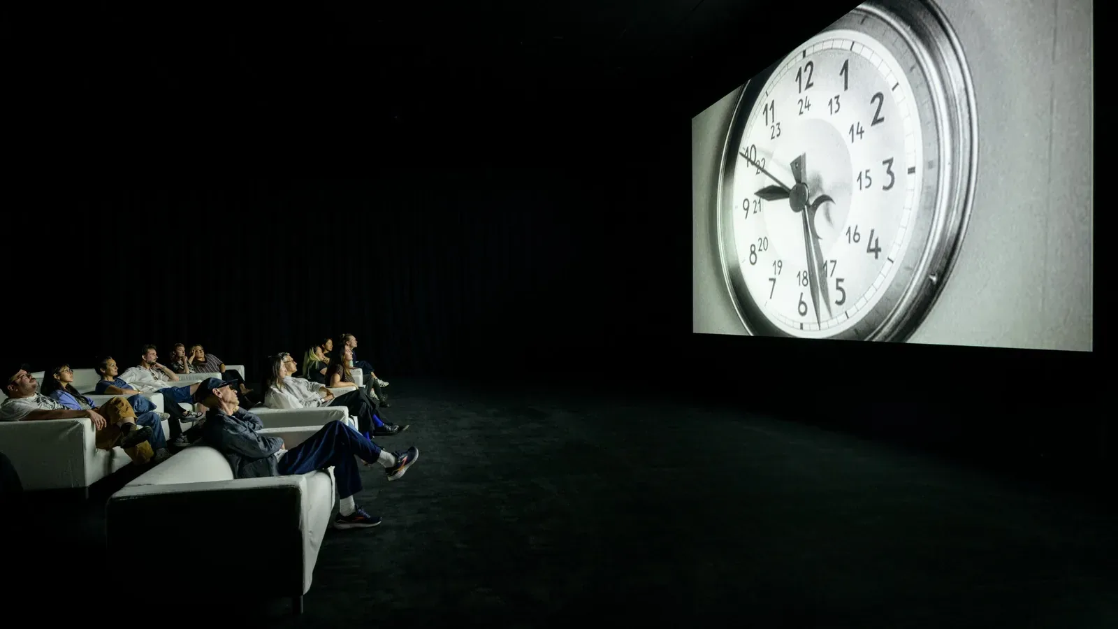 Visitors watching Christian Marclay's The Clock in a darkened gallery at LACMA