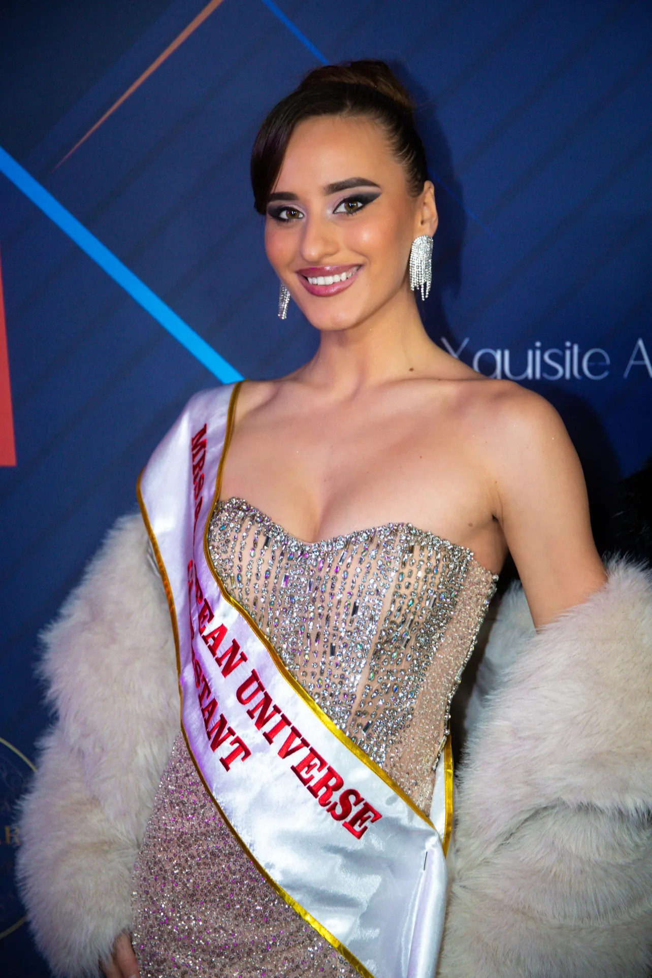 Guest in a beaded gown and pageant sash with a fur stole