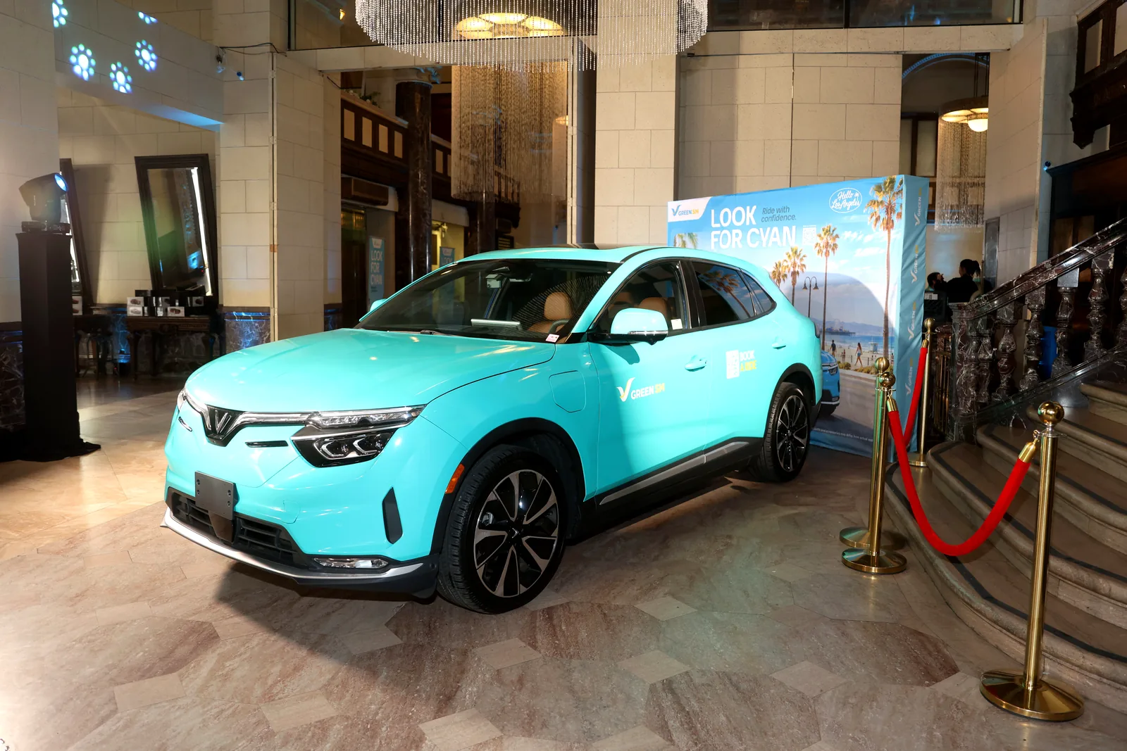 A cyan Green SM VinFast VF 8 displayed beside a Look for Cyan backdrop inside The Majestic Downtown