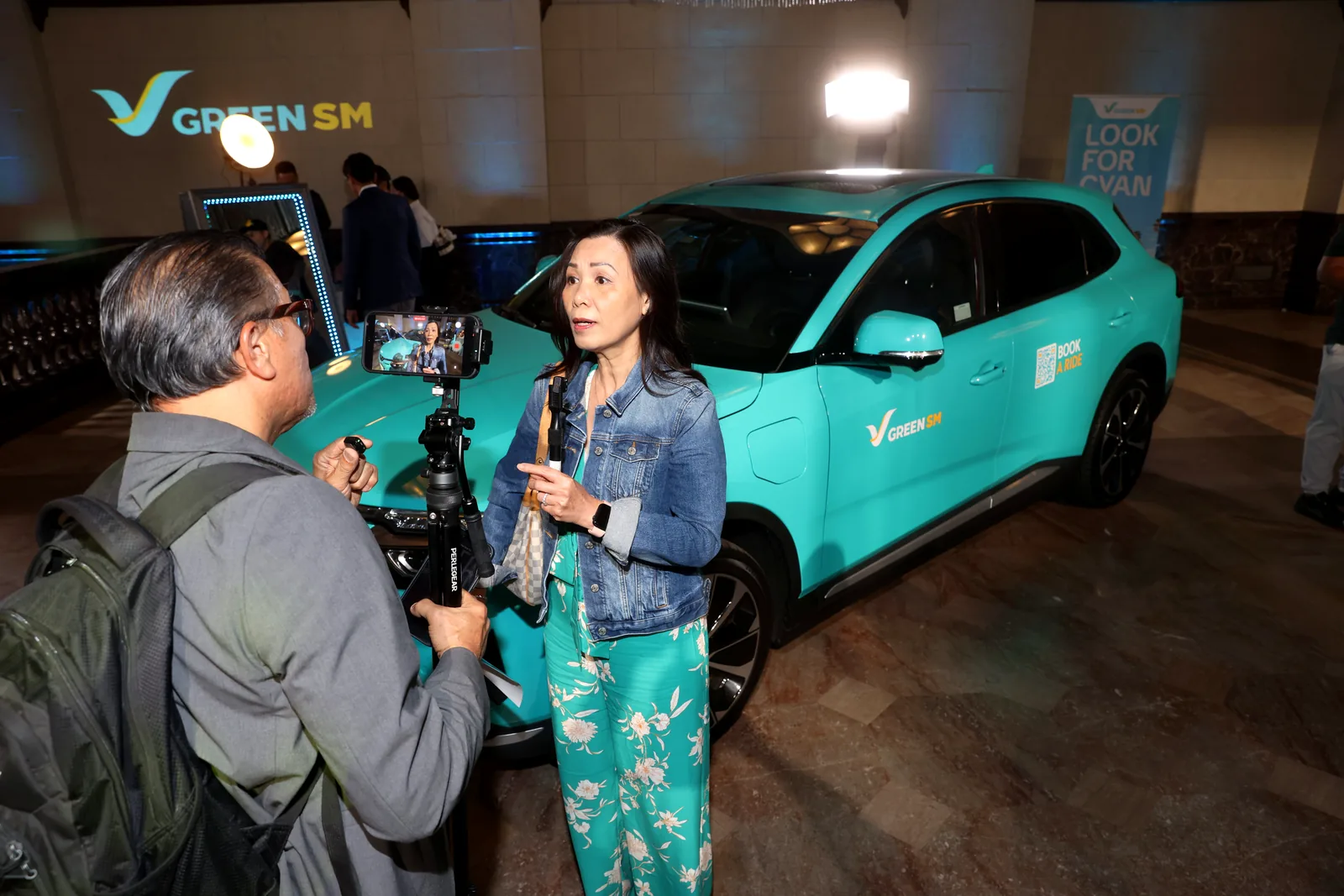 A Green SM spokesperson being interviewed on camera next to a cyan VinFast VF 8 at the launch