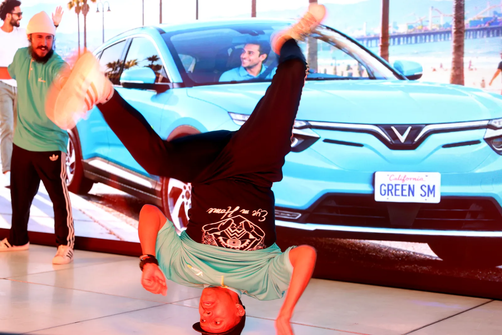 A breakdancer performing a headstand in front of a Green SM screen at the launch