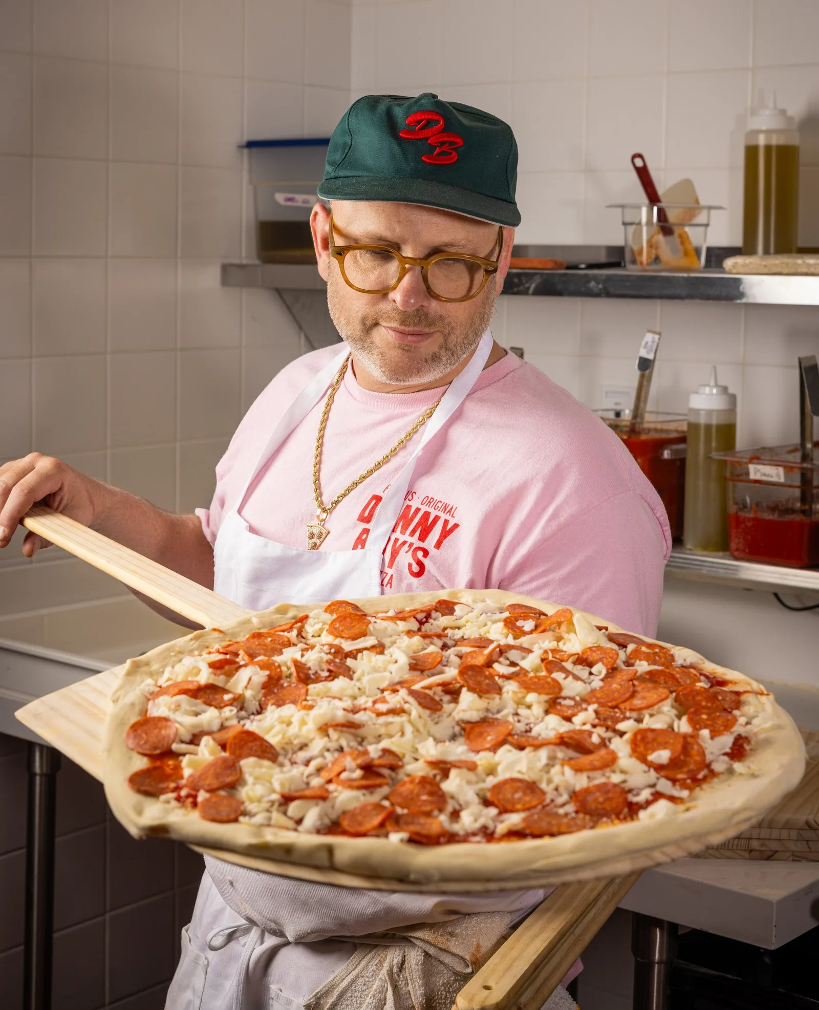 Man in a cap holding a pepperoni pizza on a wooden peel