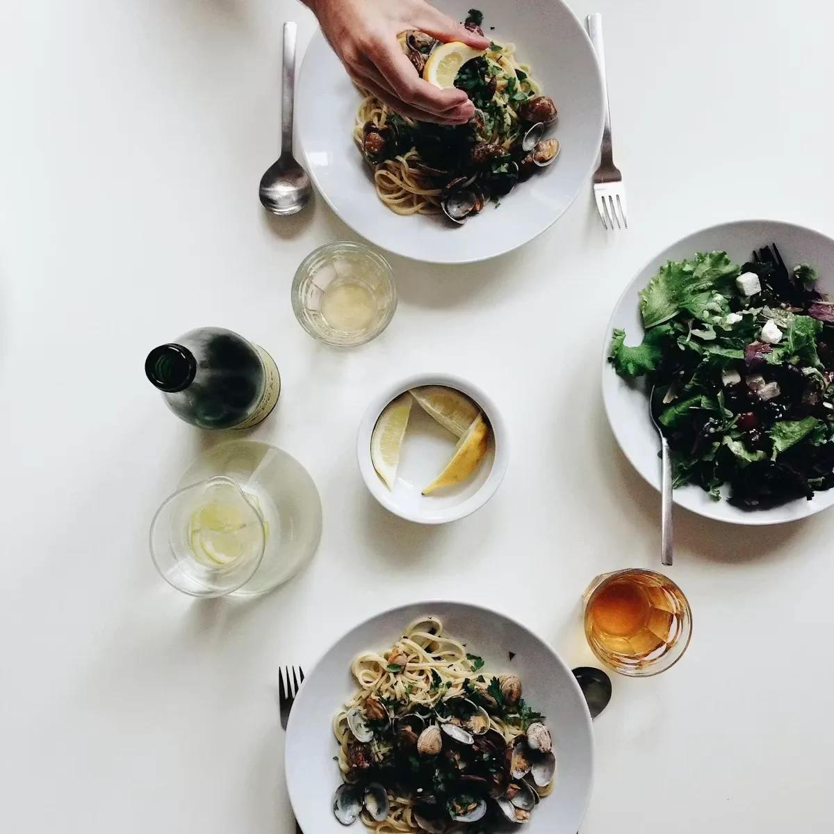 Overhead of pasta, greens, a wine bottle and glasses on a white table