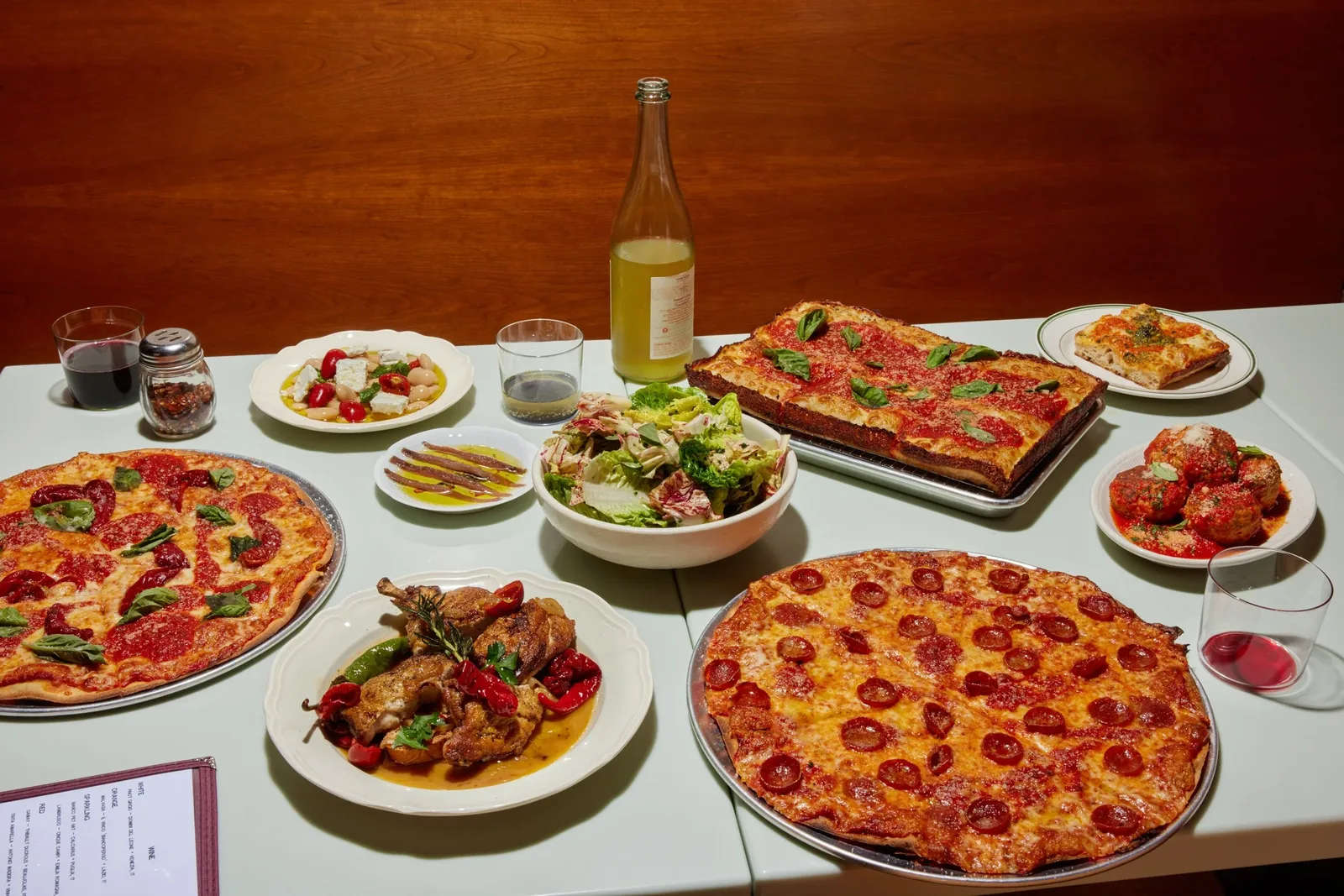 Table of square pan pizzas, salad, meatballs and a wine bottle