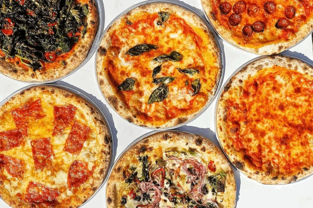 Five whole pizzas with different toppings on a white surface