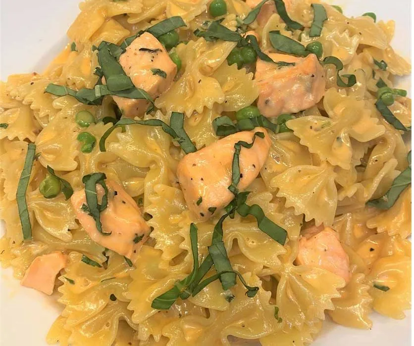 Bow tie pasta with salmon, peas and basil on a white plate