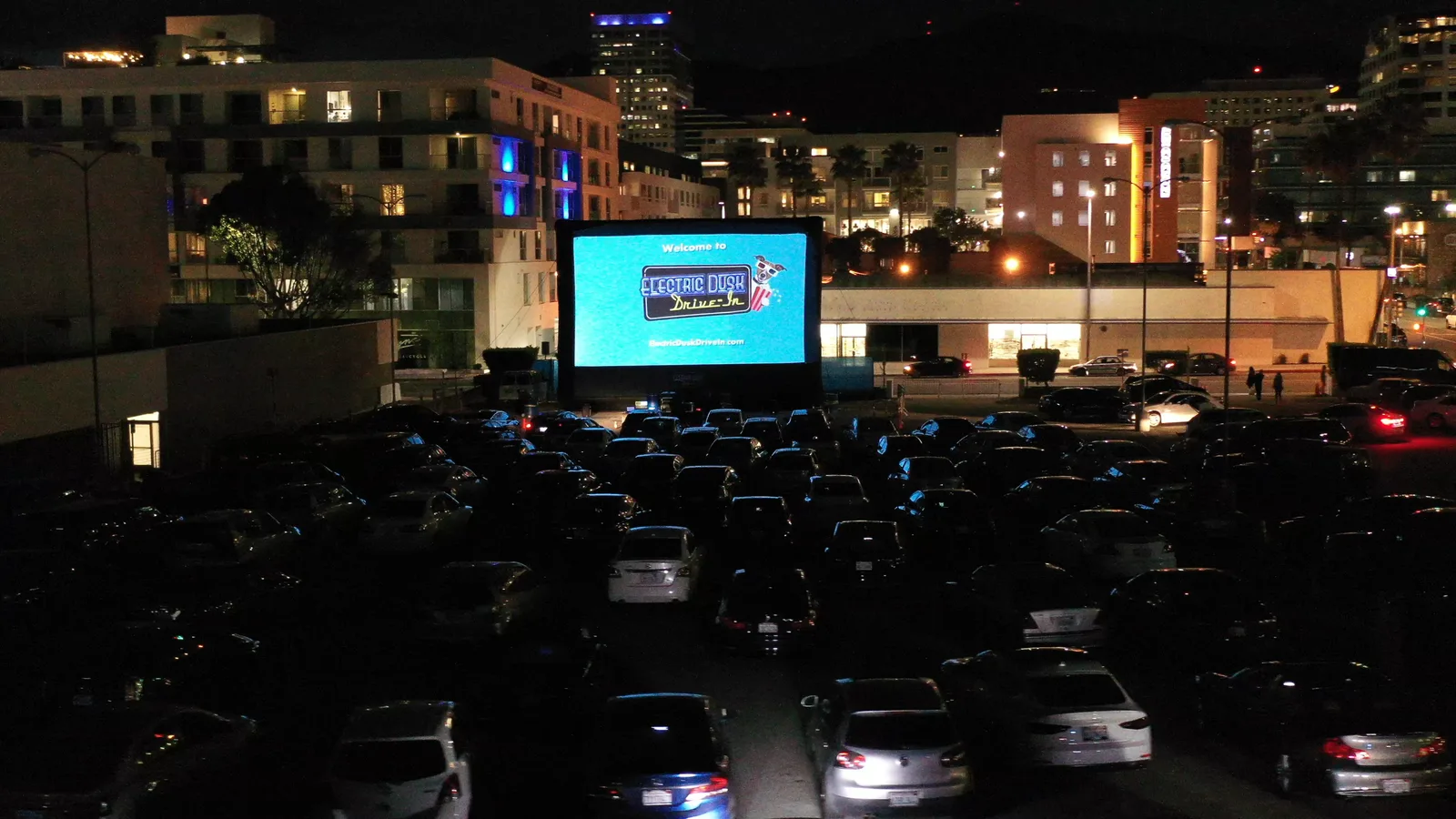 Cars parked before a giant outdoor movie screen under the night sky at the Electric Dusk Drive-In in Glendale