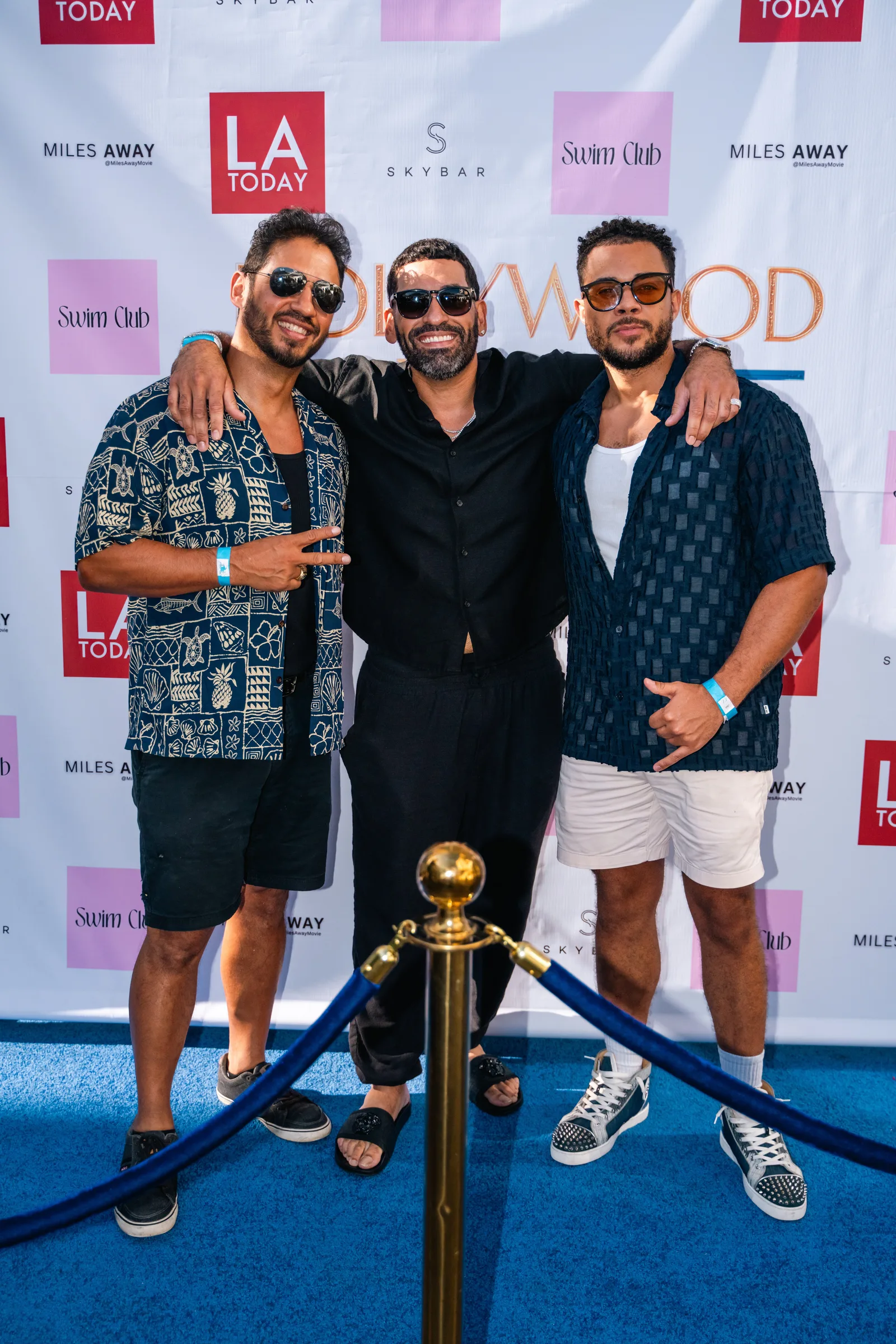 Three guests pose arm in arm behind a gold globe rope post