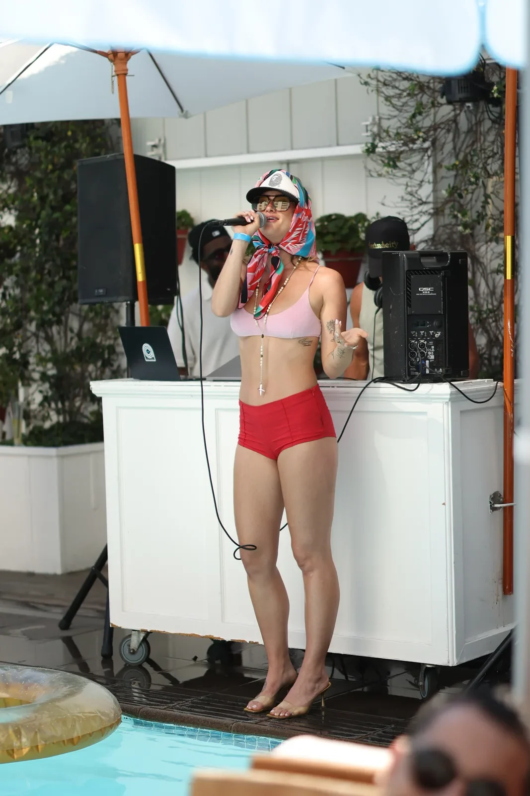 Performer in swimwear sings into a microphone next to the DJ booth
