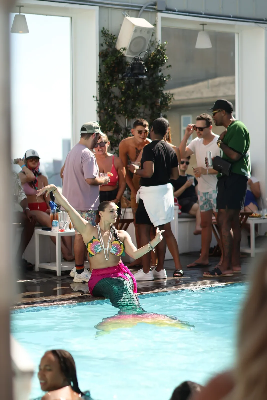 Performer in a mermaid tail in the pool as guests watch from the deck