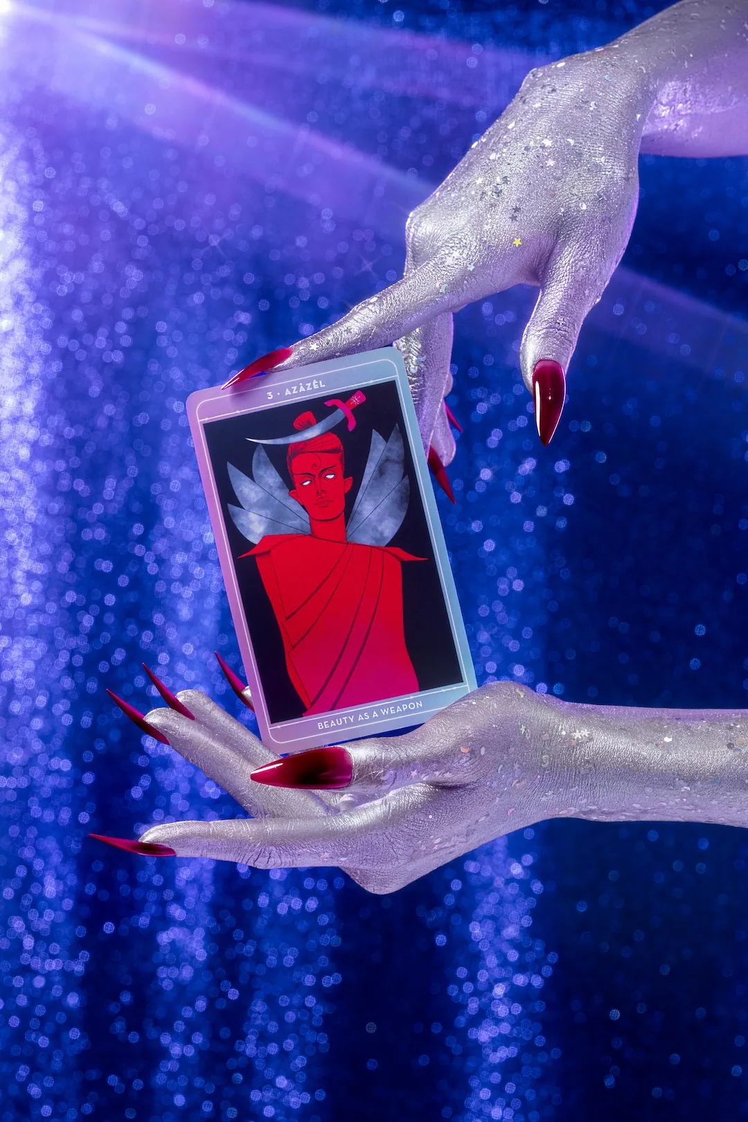 Silver-painted hands holding a single Be Not Afraid card, Azazel, Beauty as a Weapon